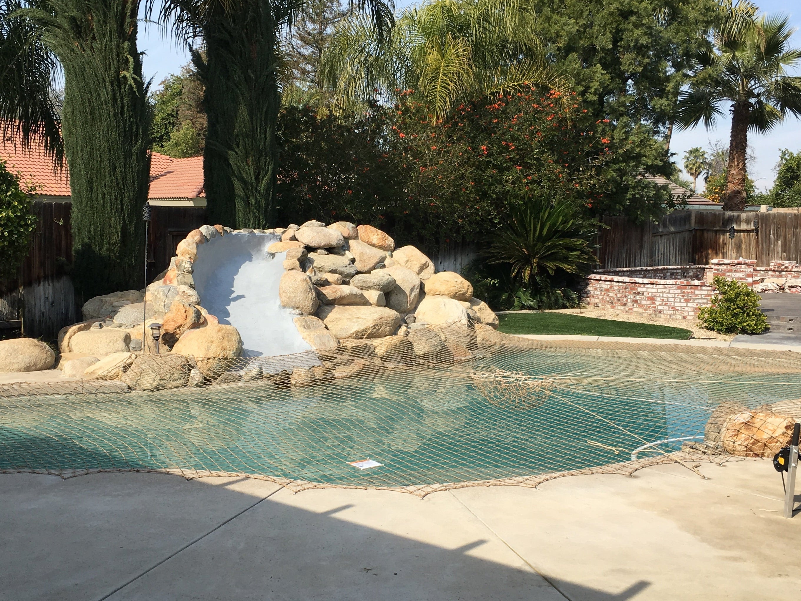 Pool with rock formation and water feature in a backyard setting and pool net